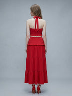 Back view of a woman in a red halter neck crop top and tiered maxi skirt.