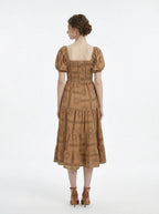 Back view of a woman in a tan midi dress with a smocked bodice and puff sleeves, showcasing the all-over print.