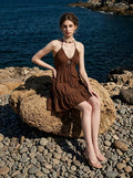 Woman in a brown halter neck tiered mini dress sitting on beach rocks