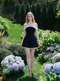Woman in a black off-the-shoulder dress with white trim walking in a garden with hydrangeas