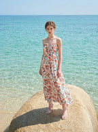 Woman standing on a rock in the ocean wearing a white floral print maxi dress with a halter neckline.