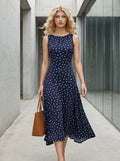 Woman walking in a navy blue polka dot midi dress holding a brown tote bag