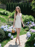 Woman in a white floral print mini dress walking on a garden path.
