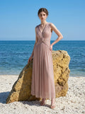 woman in a rose gold metallic a-line maxi dress with a v-neckline and ruched empire waist standing by a rock at the beach
