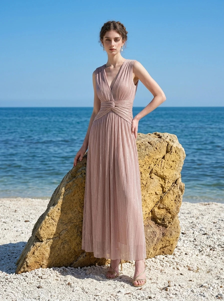 woman in a rose gold metallic a-line maxi dress with a v-neckline and ruched empire waist standing by a rock at the beach