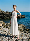 Woman wearing a white halter neck midi dress on a rocky shore