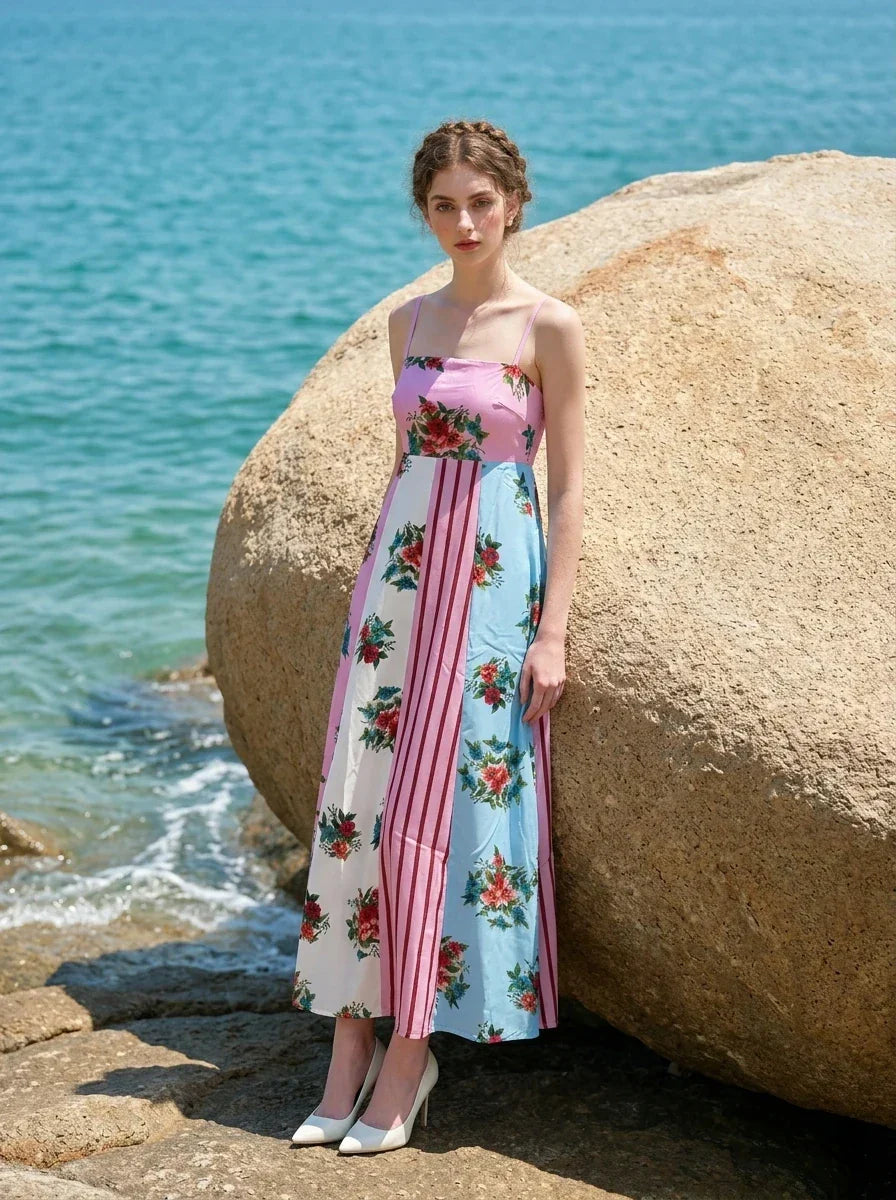 Woman leaning against a large rock on a beach, wearing a colorblock floral print maxi dress