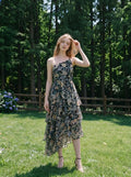 Woman posing in a grassy area wearing a floral print one-shoulder chiffon dress with a tiered, asymmetrical ruffle skirt.