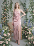Woman in a dusty rose satin one-shoulder maxi dress with a high slit, posing in a floral garden setting.