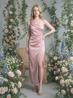 Woman in a dusty rose satin one-shoulder maxi dress with a high slit, posing in a floral garden setting.