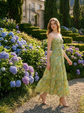 Woman in a green floral print strapless maxi dress walking in a garden with blue hydrangeas.