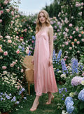 Woman posing in a floral garden wearing a pink satin slip dress.