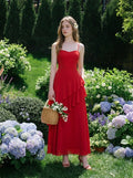 Woman in a red, floor-length, spaghetti strap dress with ruffle detailing, holding a wicker basket of flowers in a garden