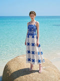 Woman wearing a pink midi dress with a tropical print and spaghetti straps on a large rock by the sea