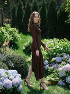 Model wearing a long-sleeved brown ruched mini dress with an asymmetrical hemline and high neckline, walking in a garden