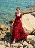 Woman sitting on rocks by the ocean wearing a red tiered tulle dress