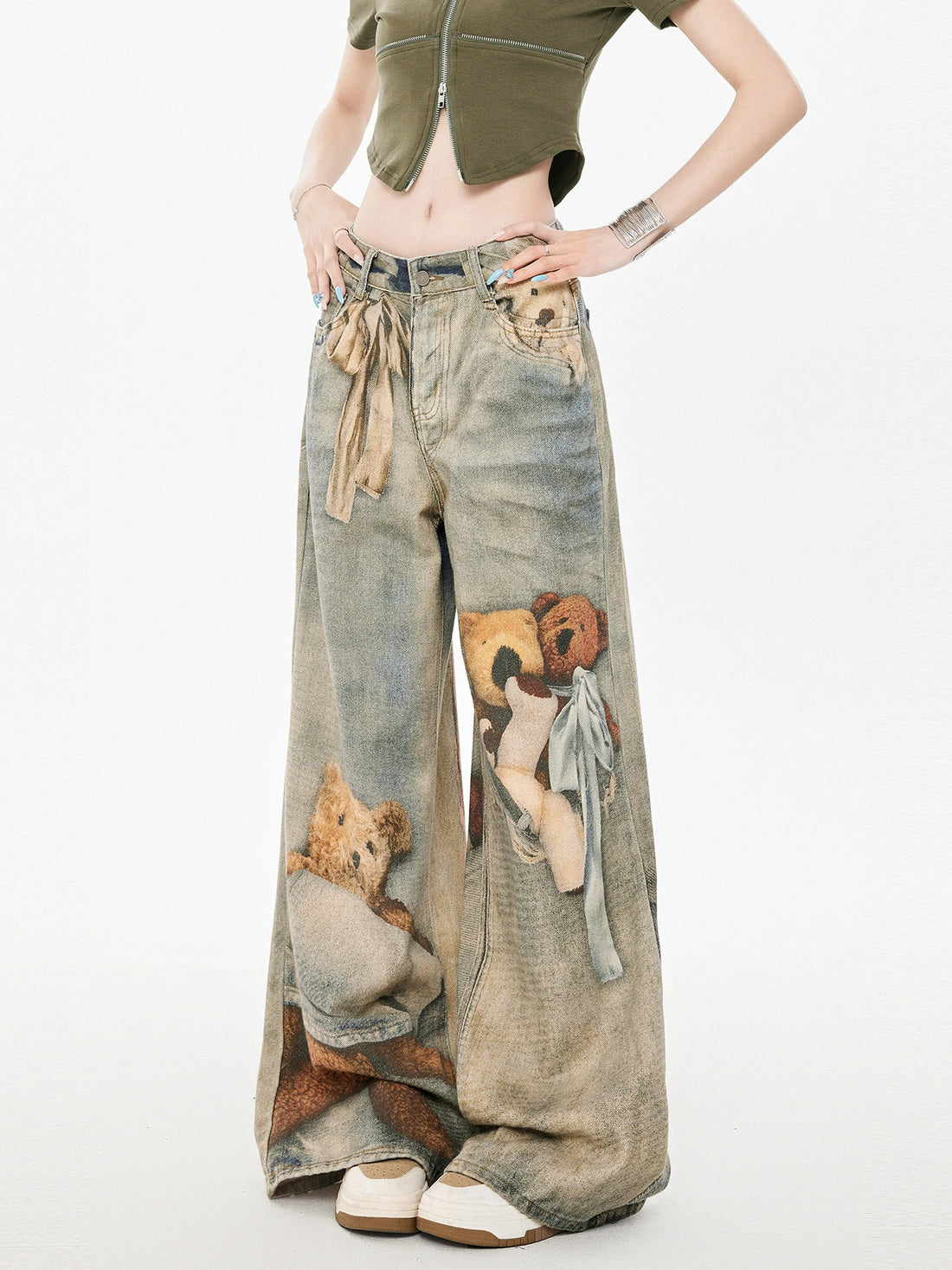 Woman wearing wide leg denim pants with teddy bear graphic print and tie waist, paired with a cropped olive green top.