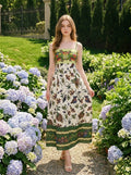 Woman wearing a white midi dress with a green smocked bodice and a colorful bird and floral print, standing in a garden with hydrangeas.