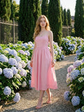 Woman wearing a pink midi dress with spaghetti straps and a square neckline, walking in a garden with hydrangeas.