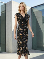 Woman walking outdoors wearing a black floral print midi dress with V-neck and lace detailing.