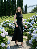 Woman in a sleeveless black A-line midi dress walking through a garden with blue hydrangeas.