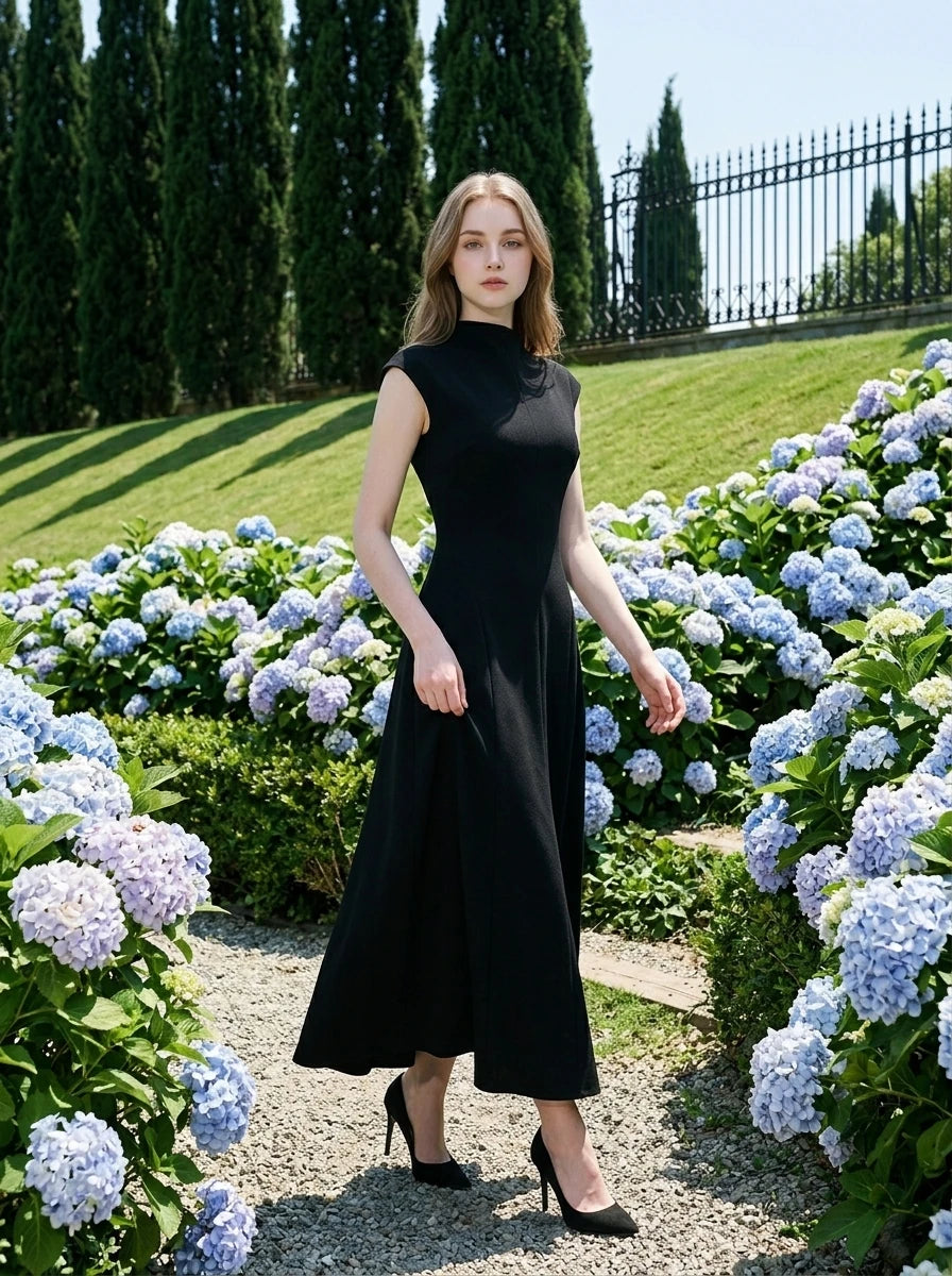 Woman in a sleeveless black A-line midi dress walking through a garden with blue hydrangeas.