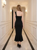 Back view of a woman in a black one-shoulder mermaid dress with a sweetheart neckline and ruched bodice, standing in a hallway.