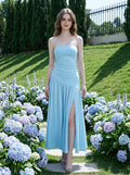 Woman wearing a sky blue strapless ruched jersey knit A-line evening dress with an asymmetrical hemline and side slit in a garden with hydrangeas