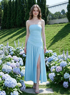 Woman wearing a sky blue strapless ruched jersey knit A-line evening dress with an asymmetrical hemline and side slit in a garden with hydrangeas