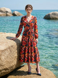 Model posing on rocks by the sea, wearing a navy blue floral print midi dress with long sleeves and a V-neck wrap style.