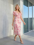 Woman walking outdoors in a pink floral print midi dress with a handbag.