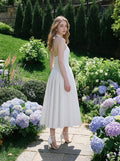 Rear view of a woman in a white halter neck midi dress amidst lush greenery.