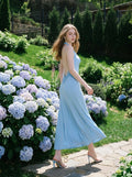 Woman turning to look over her shoulder in a light blue maxi halter dress in a garden setting with hydrangeas.