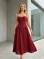Woman standing outdoors wearing a deep red linen blend midi dress with a sweetheart neckline and full skirt
