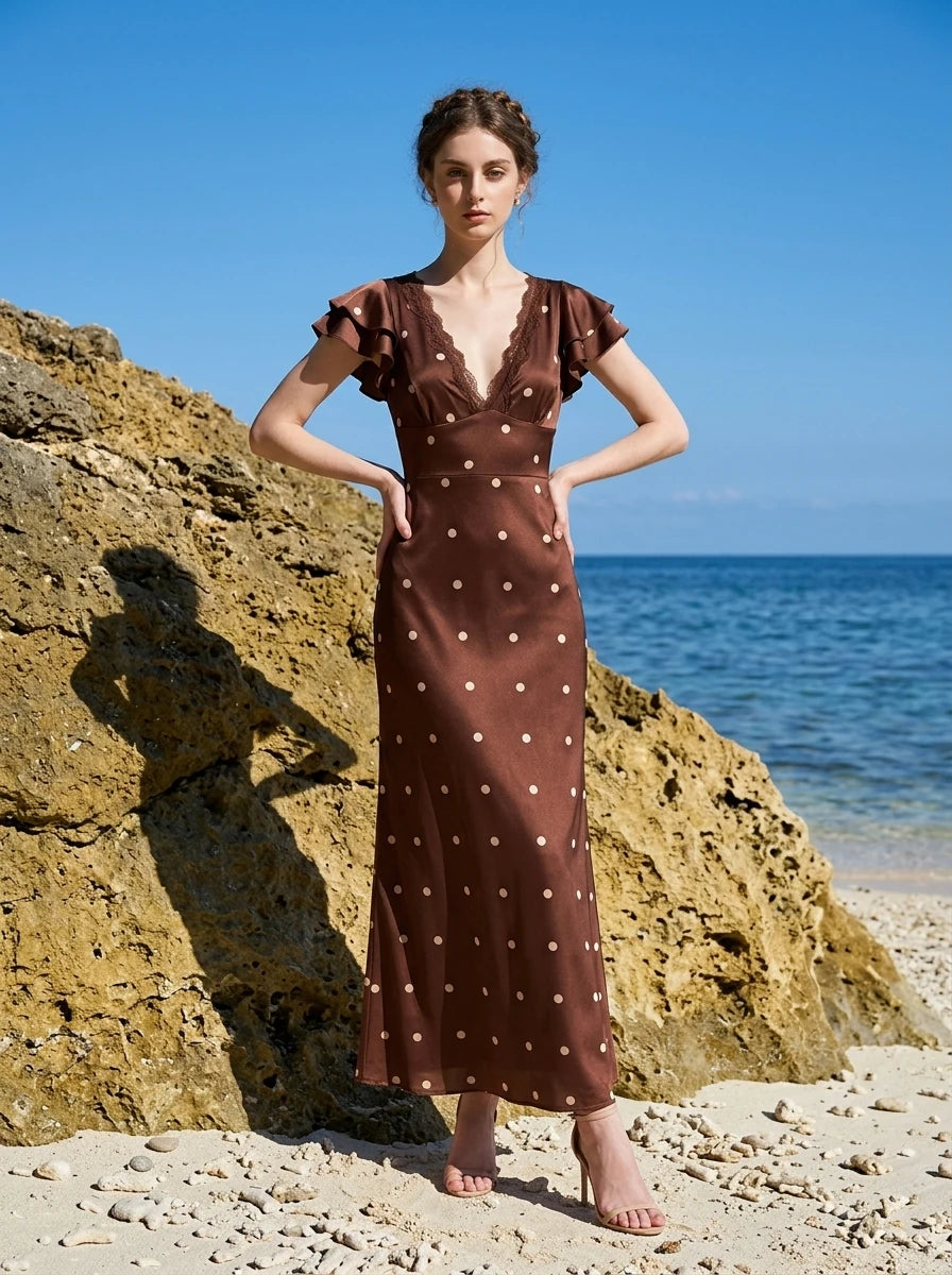 Full body shot of a woman in a brown polka dot midi dress with ruffled sleeves on a beach.