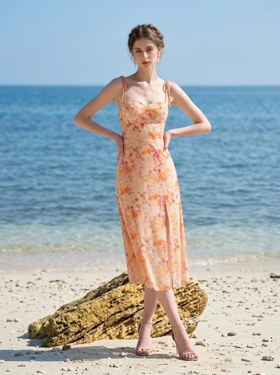 Woman in a peach floral print midi dress with side slit standing on a beach