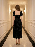 Back view of a woman in a black floral burnout velvet midi dress with puff sleeves.