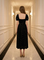 Back view of a woman in a black floral burnout velvet midi dress with puff sleeves.