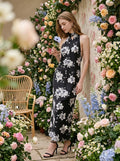 Woman posing against a floral wall in a black floral print maxi dress