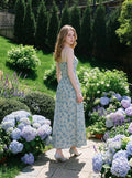 Woman standing in a garden with hydrangeas wearing a light blue floral print midi dress