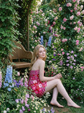Woman in a strapless pink floral embroidered mini dress sitting in a garden