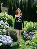 Woman in a black asymmetrical mini dress walking in a garden setting.