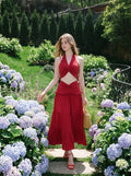 Woman in a red halter neck crop top and tiered maxi skirt walking through a garden.