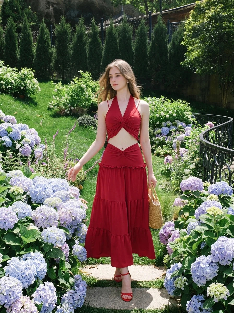 Woman in a red halter neck crop top and tiered maxi skirt walking through a garden.