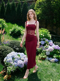 Woman walking in a garden wearing a burgundy column dress with lace detailing.