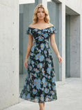 Woman standing outdoors wearing a black floral print off-the-shoulder midi dress with blue flowers