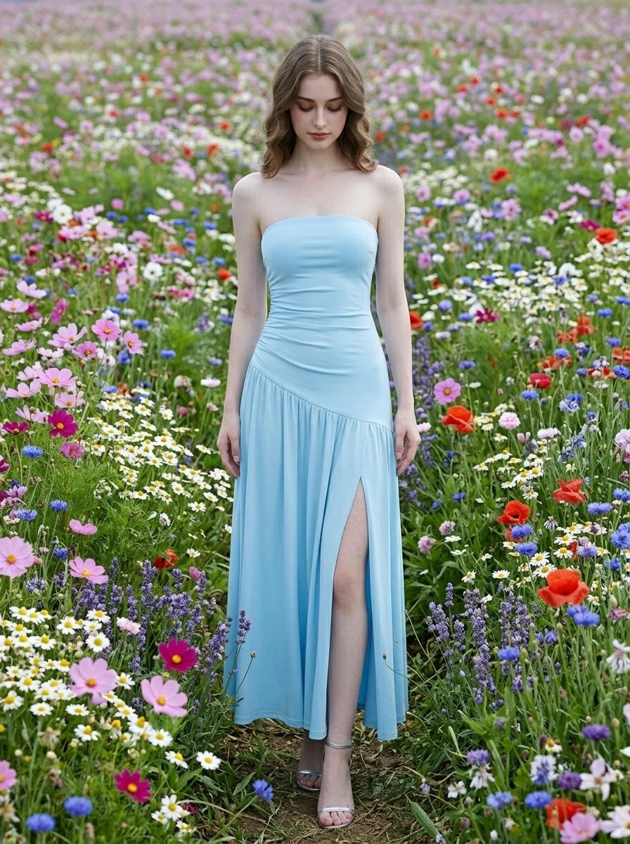 Woman wearing a sky blue strapless ruched jersey knit A-line evening dress with an asymmetrical hemline and side slit in a field of flowers