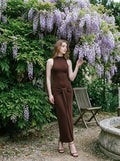 Woman in a brown sleeveless mock neck maxi dress with ruched knot detail posing in a garden
