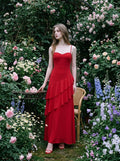Woman in a red, floor-length, spaghetti strap dress with ruffle detailing, posing in a rose garden