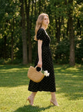 Woman walking in a park wearing a black floral burnout velvet midi dress with puff sleeves.